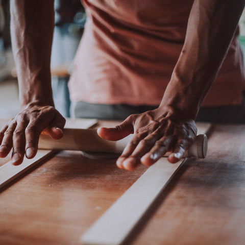 Person rolling out clay on a wooden surface with a blurred background in a pottery studio